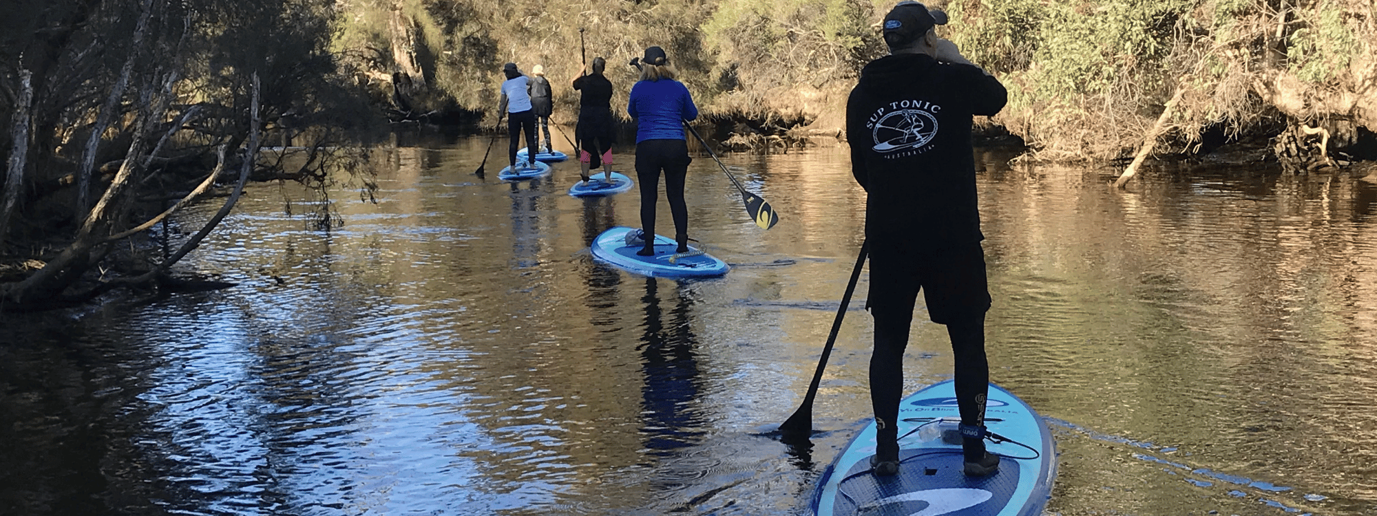 4 people on SUP boards, paddling in the shade up the Swan river.