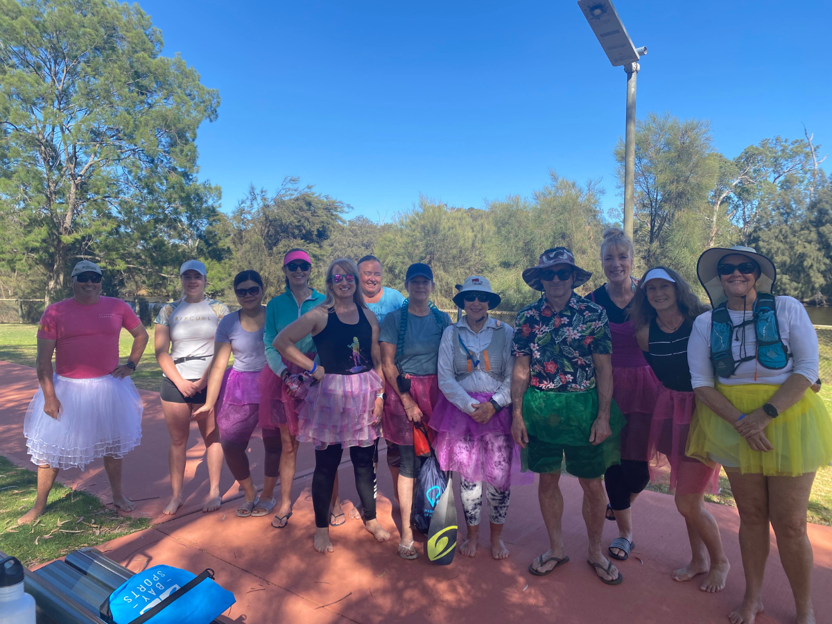 A group of 12 or so people all wearing tutu's getting ready for a fun dress up style paddle board event.